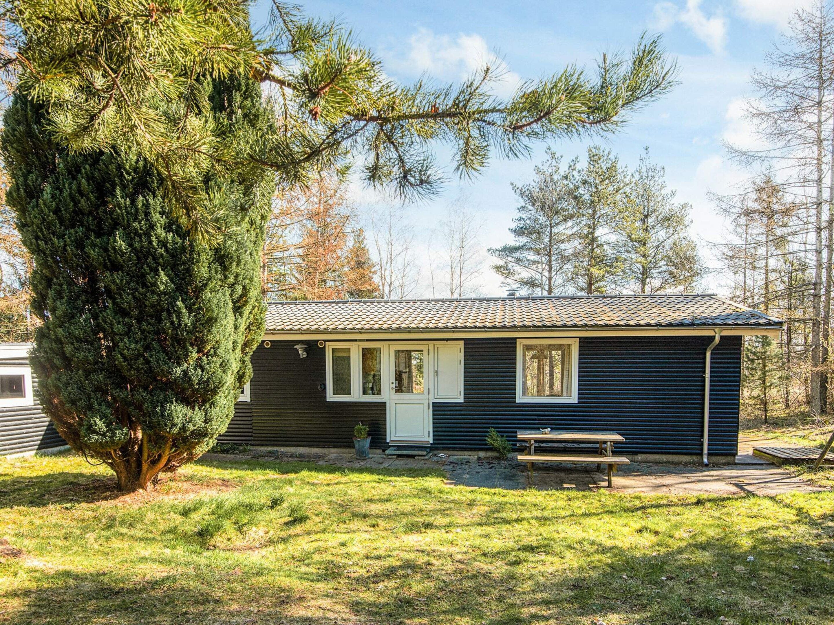 A small, single-story cabin with a tiled roof, a front door, and a bench outside.