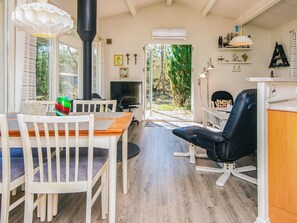A cozy room with a wooden dining table, white chairs, a black office chair, a TV, and a large window overlooking greenery.