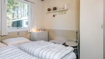 Quarto com uma cama, mesa de cabeceira, cadeira e prateleira com objetos decorativos.
