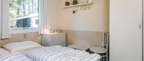 A bedroom with a bed, a nightstand, a chair, and a shelf with decorative items.