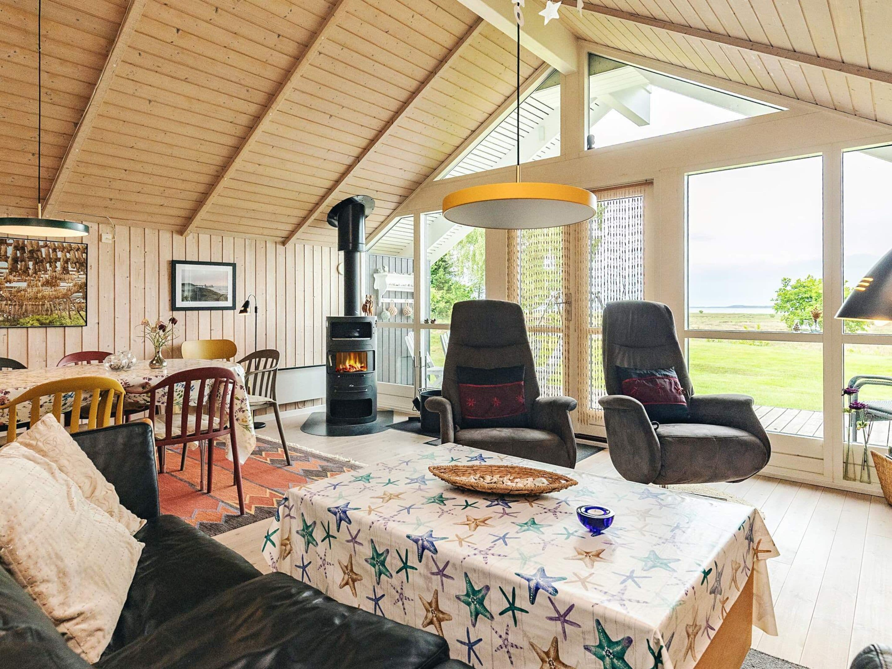 Un salon chaleureux avec une cheminée, des sièges confortables et de grandes fenêtres donnant sur l’extérieur.