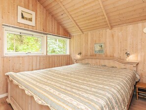 A bedroom with wooden walls, a bed with a floral-patterned bedspread, two windows, and a picture on the wall.