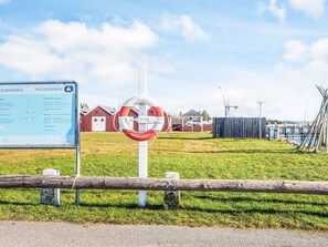 A sign with text and a lifebuoy, a wooden fence, and a grassy area with buildings in the background. - 5 Star Holiday Home in Hojslev (Hojslev)