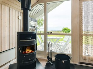 A wood-burning stove in a room with a view of a grassy field and a wooden deck outside. - 5 Star Holiday Home in Hojslev (Hojslev)