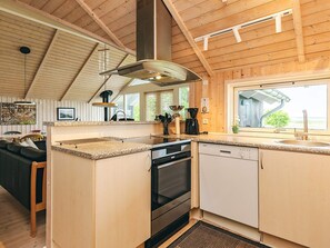 A kitchen with wooden cabinets, a stove, a dishwasher, and a window with a view. - 5 Star Holiday Home in Hojslev (Hojslev)