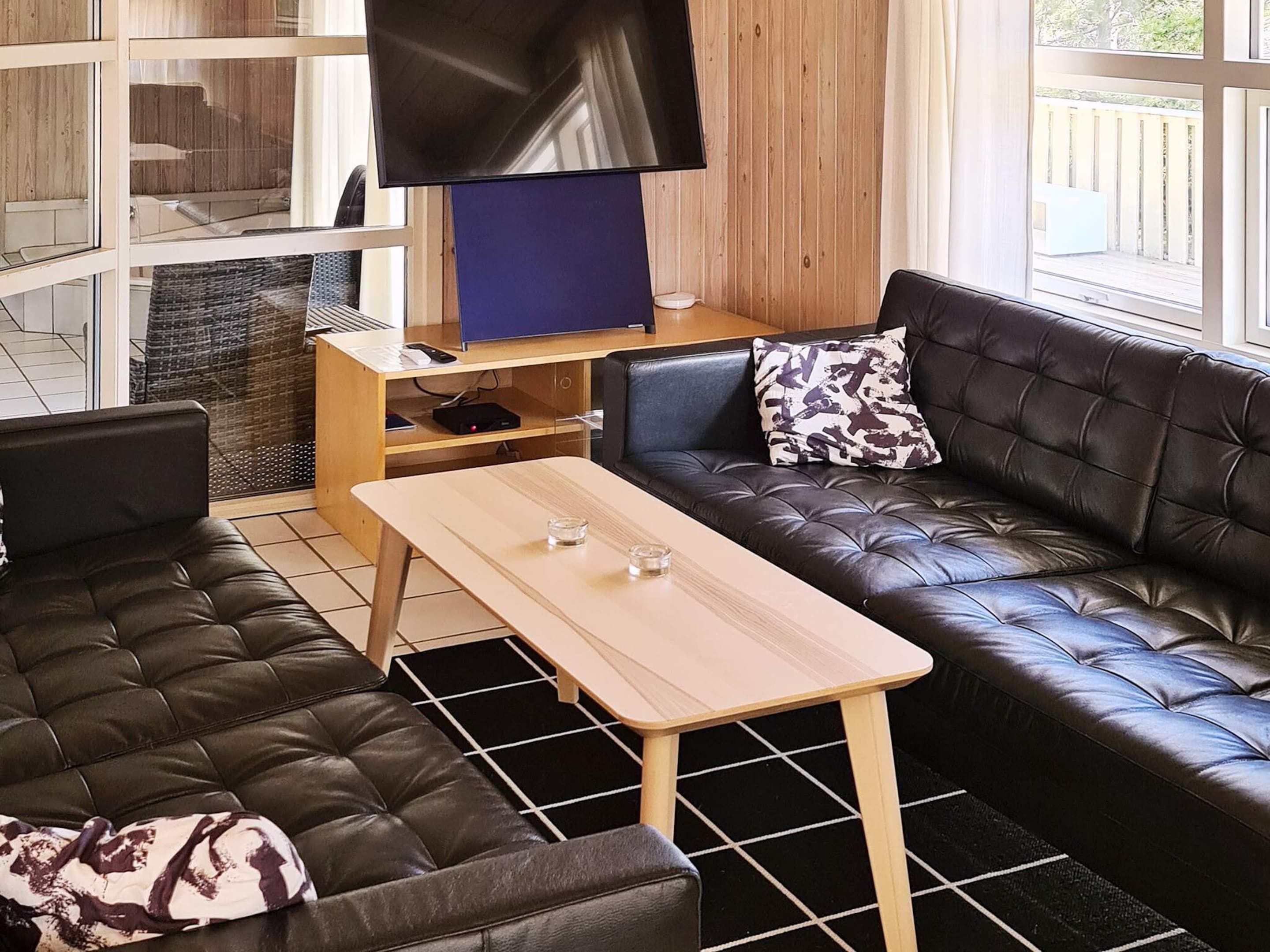 A modern living room with a leather sofa, a wooden coffee table, and a flat-screen TV on a wooden stand.