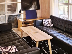 Una sala de estar moderna con un sofá de cuero, una mesa de centro de madera y un televisor de pantalla plana sobre un mueble de madera.