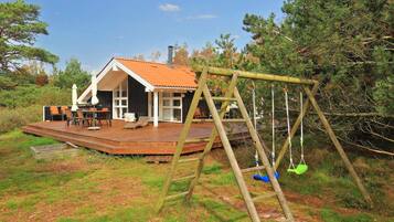 Una terraza de madera con mobiliario exterior, un columpio y una casa con techo rojo.