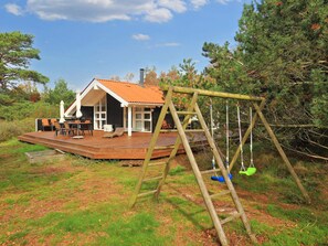 Un terrazzo in legno con mobili da esterno, un'altalena e una casa con tetto rosso.