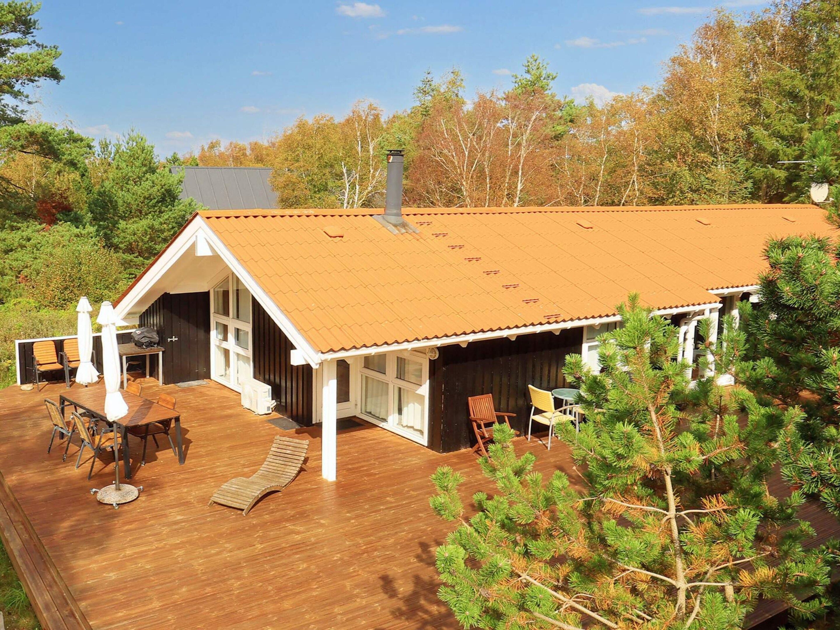 Una cabaña con terraza de madera, mobiliario exterior y una chimenea.