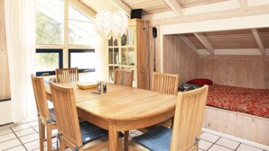 Una mesa de comedor de madera con seis sillas, una lámpara de araña y vistas al exterior a través de amplios ventanales.