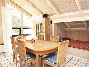 A wooden dining table with six chairs, a chandelier, and a view of the outdoors through large windows.