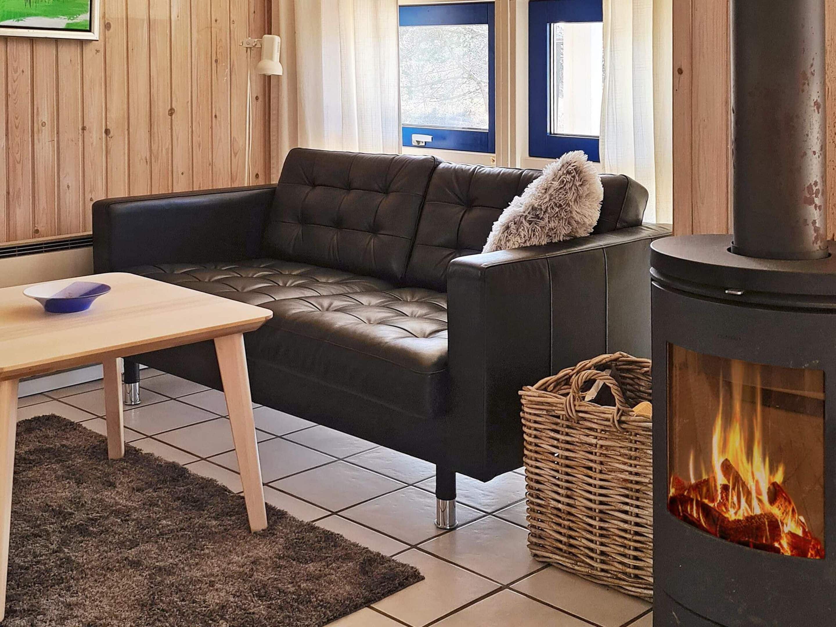 Ein gemütliches Wohnzimmer mit Ledersofa, einem kleinen Holztisch, einem Korbwannenstuhl und einem Kaminofen.