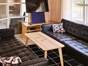 A modern living room with a leather sofa, a wooden coffee table, and a flat-screen TV mounted on a wooden wall.