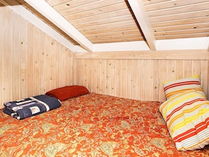 A single bed with a patterned bedspread and two pillows, a red pillow, and a striped pillow, in a room with wooden walls and a sloped ceiling. - 8 Person Holiday Home in Laeso (Læsø)