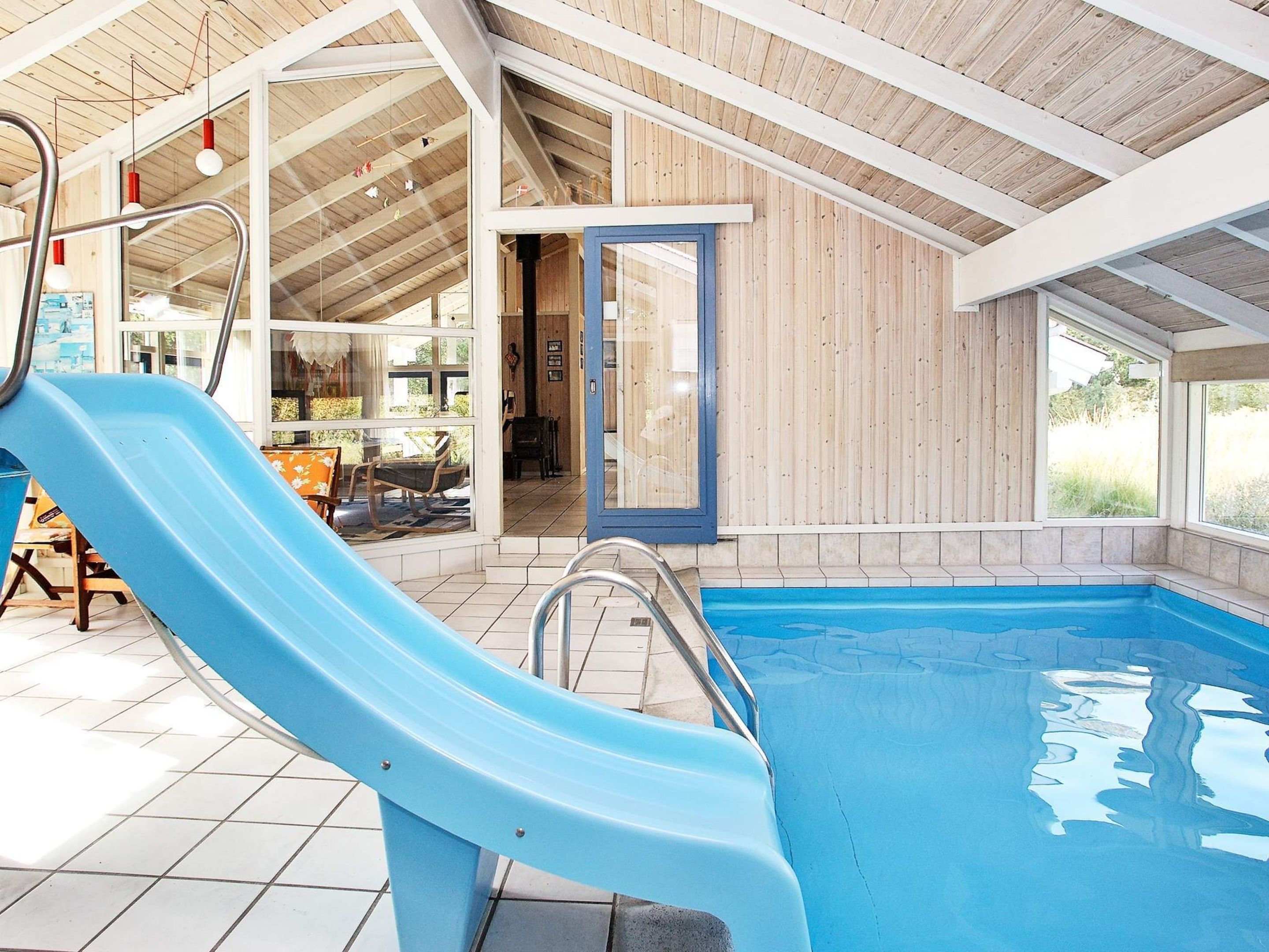 An indoor swimming pool with a blue slide, wooden walls, and a tiled floor.