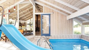 Una piscina interior con un tobogán azul, paredes de madera y suelo de baldosas.