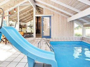 An indoor swimming pool with a blue slide, wooden walls, and a tiled floor.