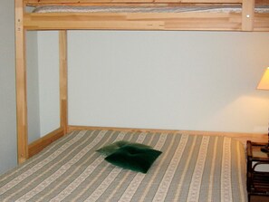 A bunk bed with a striped mattress and a pillow, a lamp on a bedside table, and a window with a view of the sky.