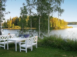 A lakeside setting with a white wooden bench and table, surrounded by trees and a calm body of water. - Holiday Home in Åtvidaberg (Atvidaberg)