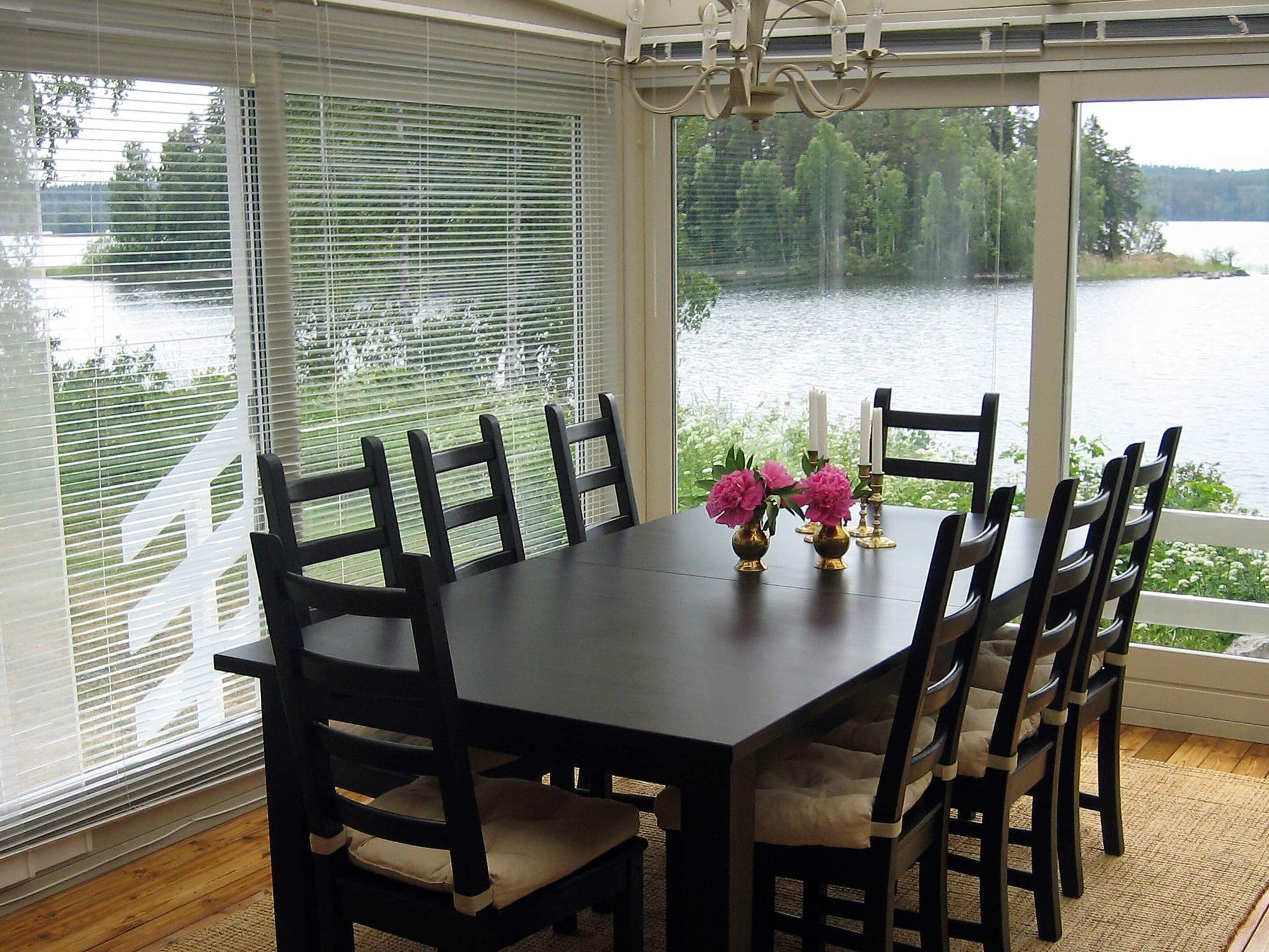 A dining table with chairs, a chandelier, and a view of a lake through large windows.