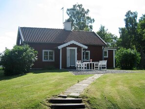 A red house with a tiled roof, a front porch with white chairs, and a stone pathway leading to the door. - Holiday Home in Åtvidaberg (Atvidaberg)