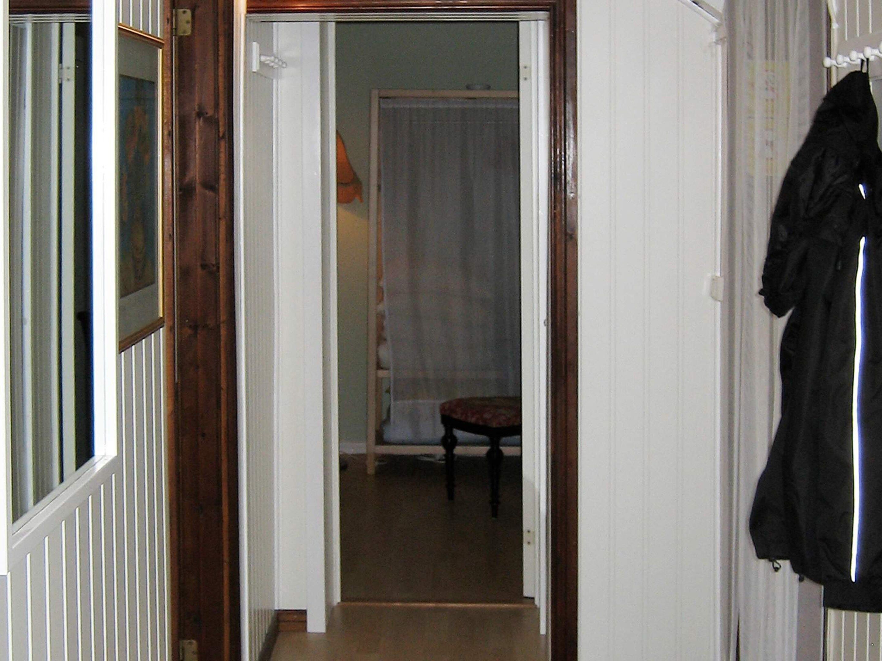 Un couloir étroit avec une porte donnant sur une pièce où se trouvent une chaise et un rideau.