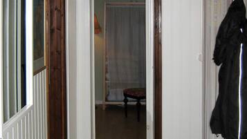 Un couloir étroit avec une porte donnant sur une pièce où se trouvent une chaise et un rideau.