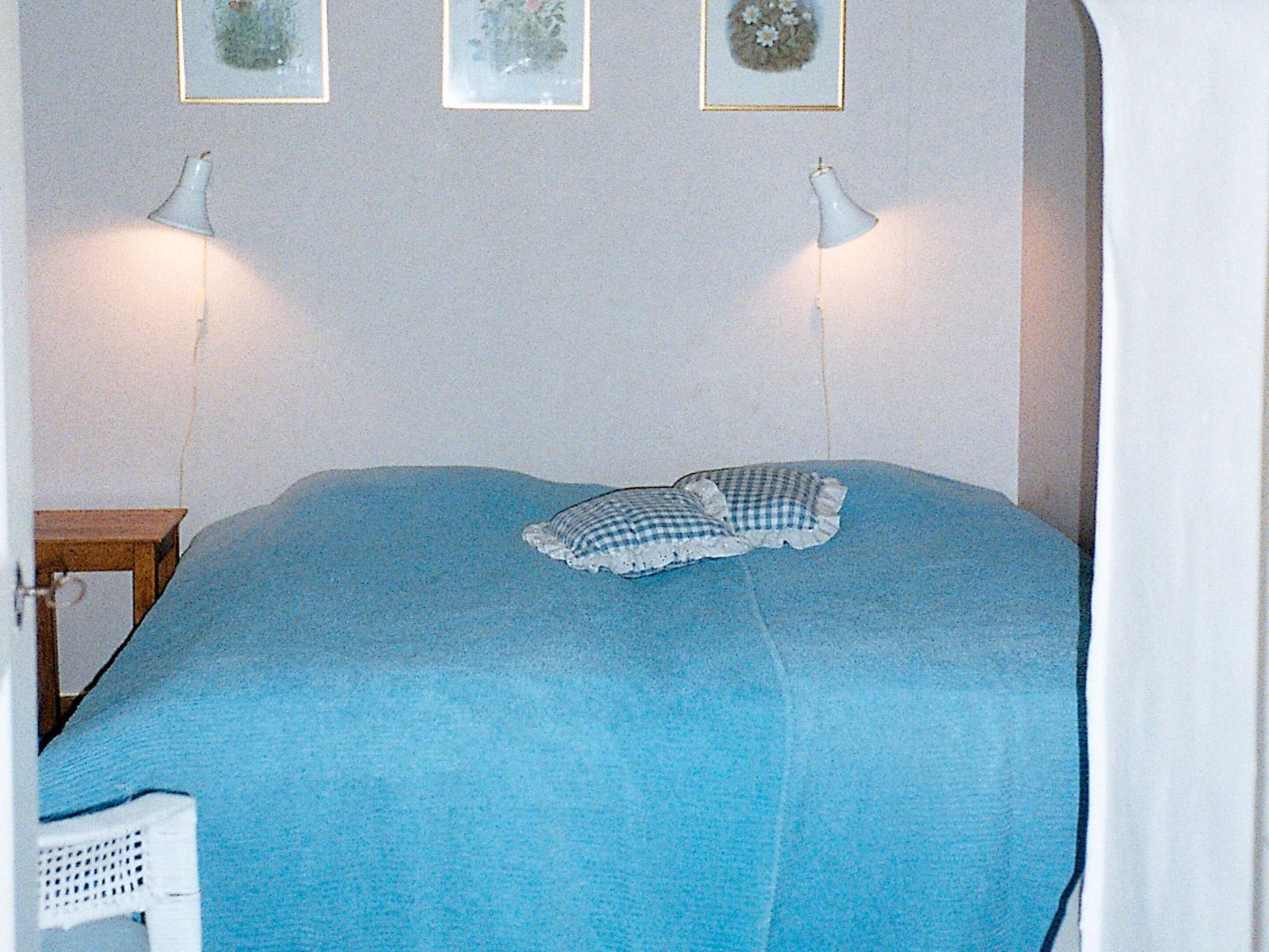 A bed with a blue blanket, two bedside lamps, and three framed pictures on the wall.