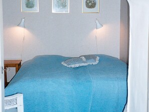 A bed with a blue blanket, two bedside lamps, and three framed pictures on the wall. - Holiday Home in Åtvidaberg (Atvidaberg)