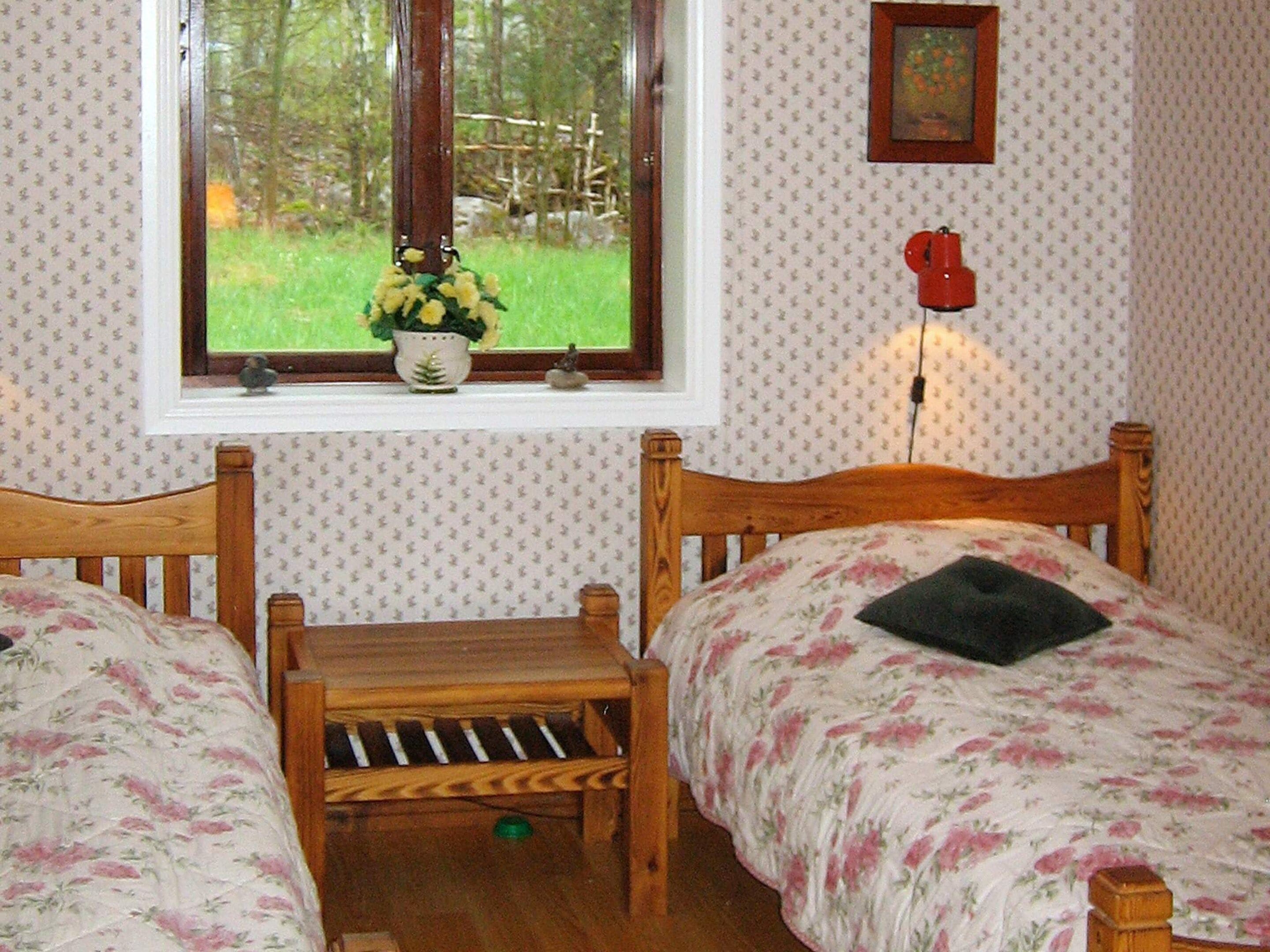 Une chambre avec deux lits en bois, une fenêtre donnant sur un paysage verdoyant, une petite table et un téléphone fixé au mur.