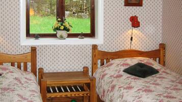 Une chambre avec deux lits en bois, une fenêtre donnant sur un paysage verdoyant, une petite table et un téléphone fixé au mur.