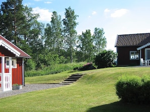 A red building with a white porch and a stone staircase leading to a grassy area. - Holiday Home in Åtvidaberg (Atvidaberg)