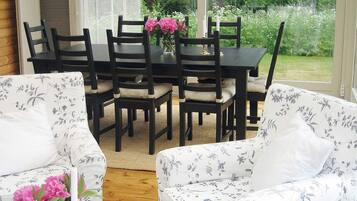 A dining area with a table and chairs, a window with a view of greenery, and floral-patterned sofas.