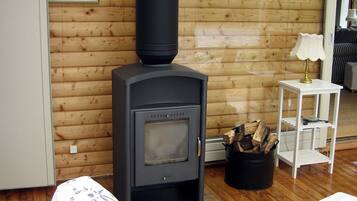 Een kamer met een zwarte houtkachel, een witte lamp op een klein tafeltje en een houten vloer.