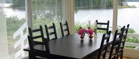 A dining table with six chairs, a chandelier, and a view of a lake through large windows with blinds.