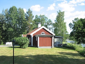 A small red wooden house with a large window and a chimney, surrounded by a grassy yard and trees. - Holiday Home in Åtvidaberg (Atvidaberg)
