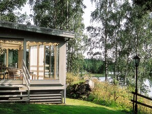 A cabin with a porch, a view of a lake, and a forested area. - Holiday Home in Åtvidaberg (Atvidaberg)