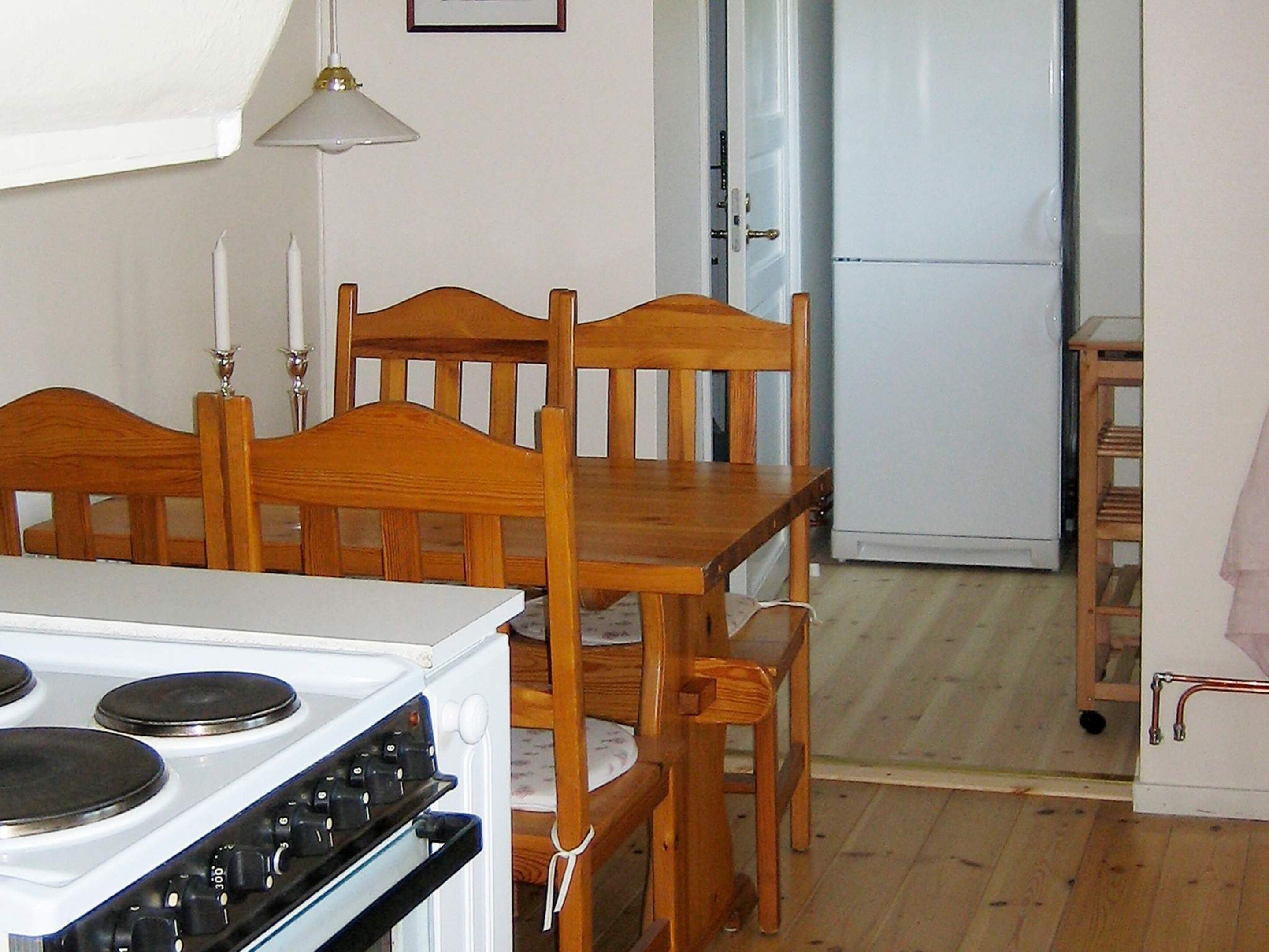 Une cuisine équipée d’une cuisinière, de chaises en bois, d’une table et d’un réfrigérateur.