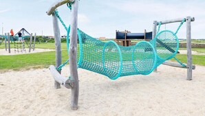 A playground with a turquoise net swing set and a slide in the background. - Spacious Holiday Home in Jutland near North Sea (Ulfborg)