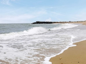 A beach with waves crashing onto the shore, a rocky outcrop in the background, and a clear sky.