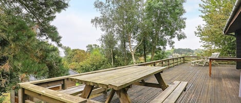 A wooden deck with picnic tables and chairs, surrounded by trees and a view of the landscape.
