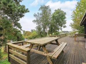 A wooden deck with picnic tables and benches, surrounded by trees and a view of the landscape. - 6 Person Holiday Home in Rudkobing (Rudkobing)
