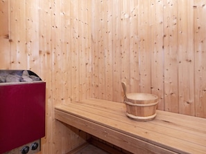 A sauna room with wooden walls, a bench, and a red sauna heater.