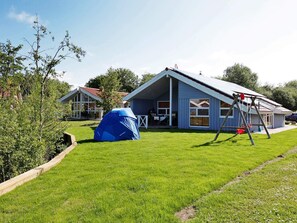 A house with a large deck, a swing set, and a blue tent in the yard.