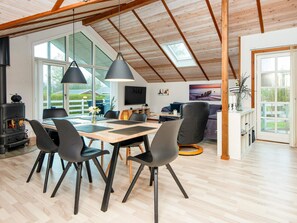 A spacious room with a high ceiling, a dining area with a wooden table and chairs, a sofa, and a fireplace. - 4 Star Holiday Home in Hemmet (Hemmet)