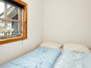 A small, single-bed room with a wooden window frame, a white wall, and a vase with white flowers on the windowsill. - 4 Star Holiday Home in Hemmet (Hemmet)