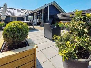 Un área de patio con mobiliario exterior, una jardinera de madera y plantas en macetas.