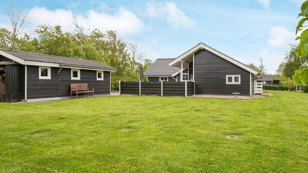 A residential property with a large grassy yard, a wooden deck, and a house with a dark exterior.