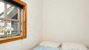 A small, single-bed room with a wooden-framed window and a vase of white flowers on the windowsill.